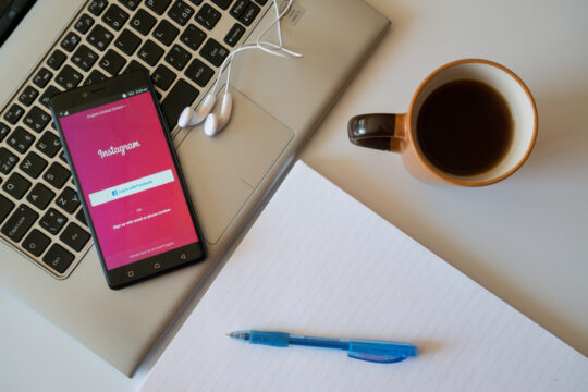 Mobile showing Instagram on a keyboard with a mug of coffee