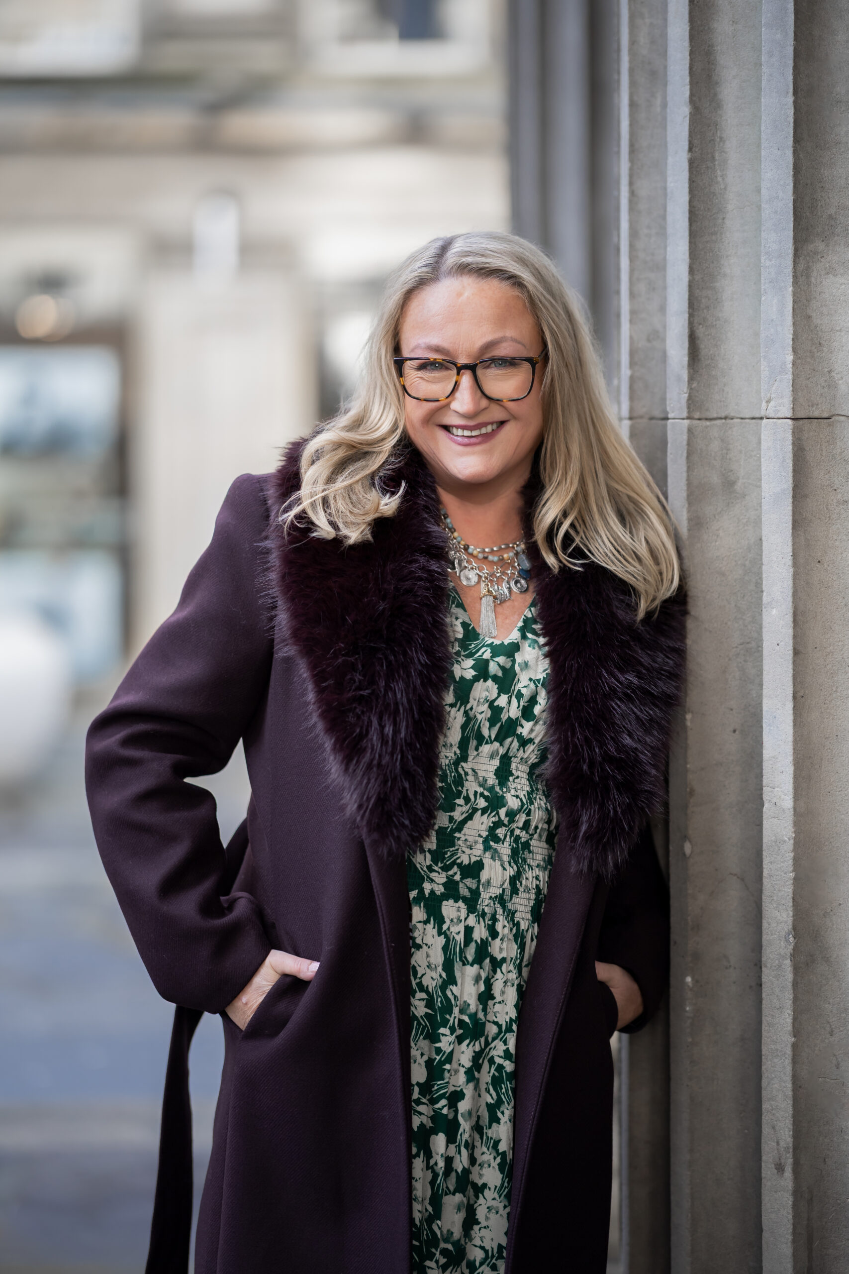 Clare Bailey wearing a burgundy coat leaning against a pillar