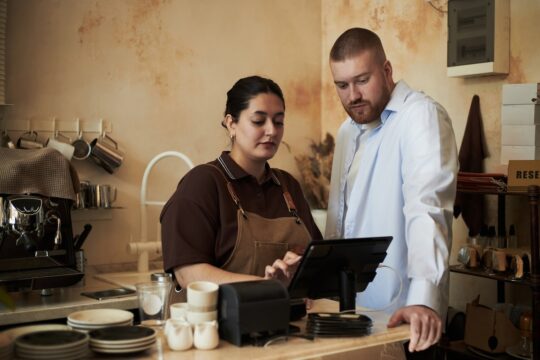 An employee helping a colleague learn to use a retail business system.